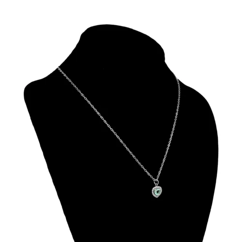 Collar plateado de acero inoxidable con dije de corazón de 1 x 1 cm, zirconia azul central y cristales exhibidor negro de busto con fondo blanco