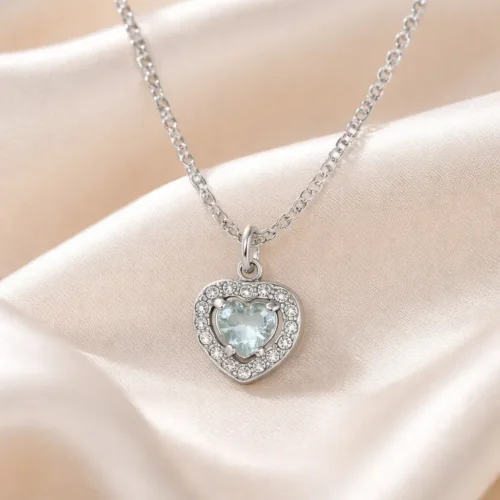 Collar plateado de acero inoxidable con dije de corazón de 1 x 1 cm, zirconia azul central y cristales sobre tela satinada cremosa