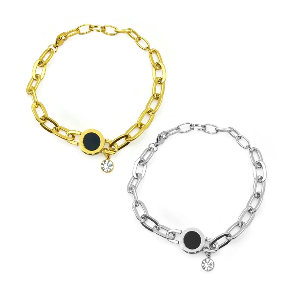 Pulsera de acero inoxidable con círculo negro, números romanos y cristal colgante en acabado dorado y plateado sobre fondo blanco