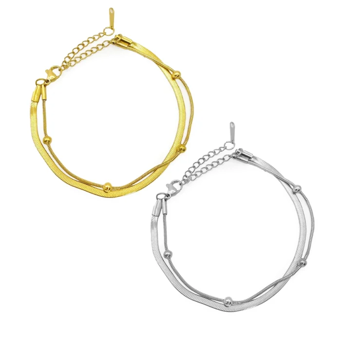 Pulsera doble de acero inoxidable con balines en acabado dorado y plateado, con cadena planchada y cadena cola de rata sobre fondo blanco