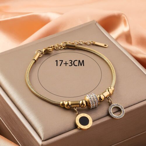 Pulsera dorada de acero inoxidable con cadena cola de rata y dijes circulares negros de resina sobre caja beige satín